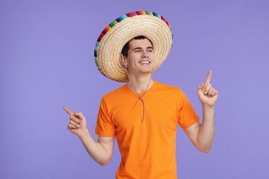 Photo of Young man in Mexican sombrero hat pointing at something on violet background