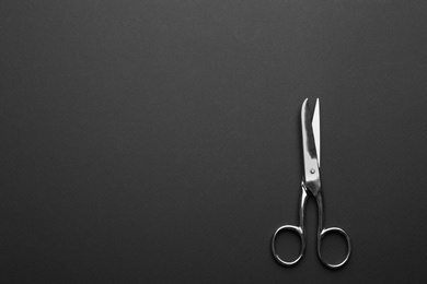 Photo of Pair of sharp scissors on dark background, top view. Space for text