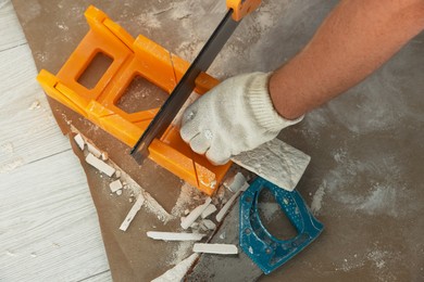 Photo of Worker cutting decorative wall tile indoors, closeup