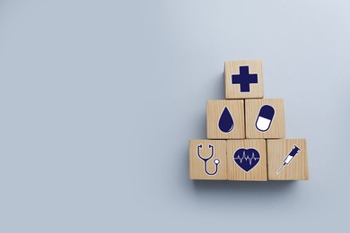 Wooden cubes with different icons on light grey background, flat lay. Insurance concept