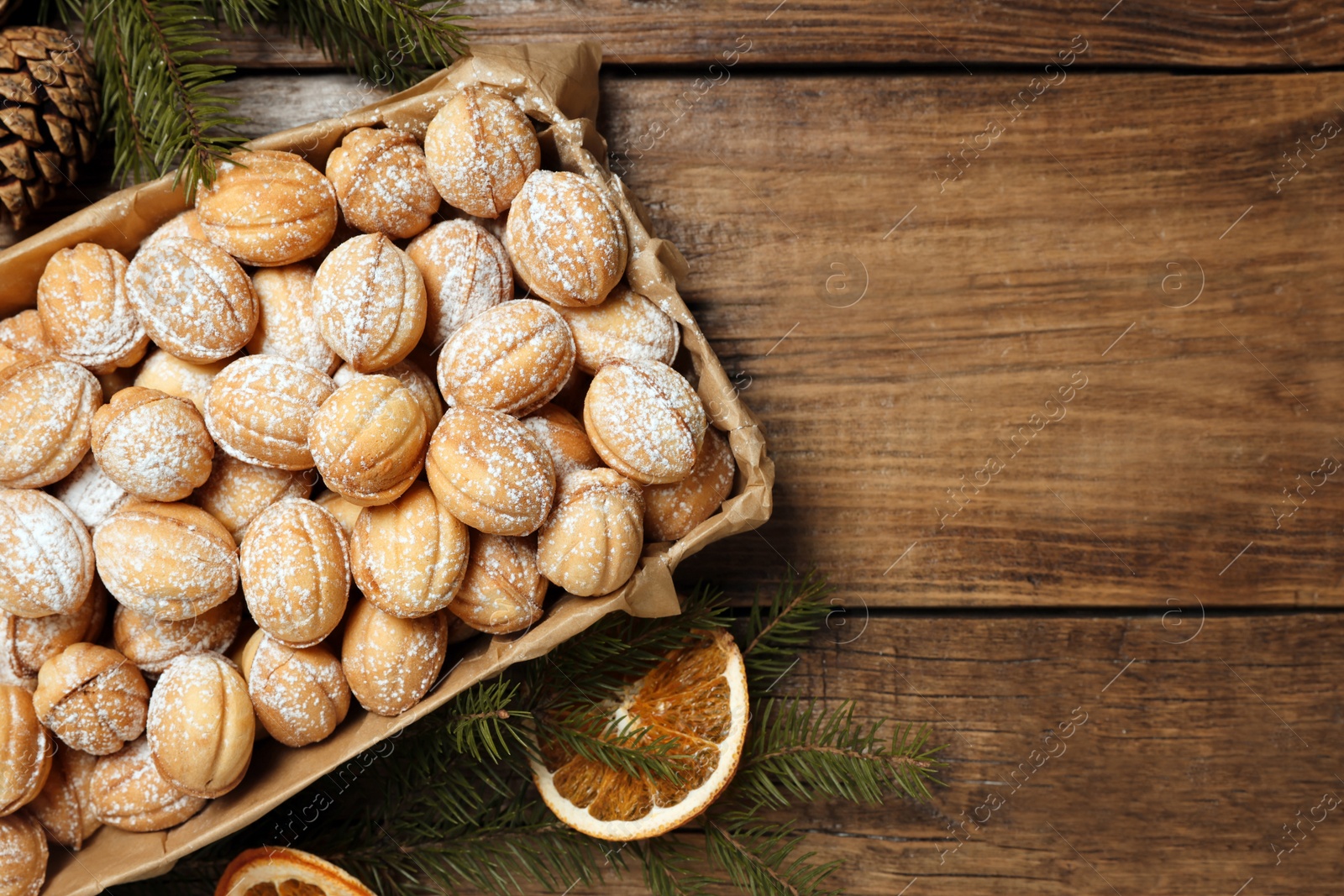 Photo of Delicious nut shaped cookies with boiled condensed milk, dry orange slices and fir tree branches on wooden table, flat lay. Space for text