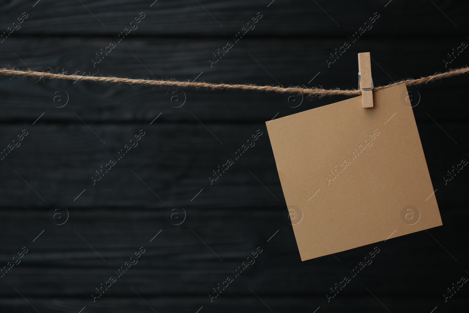 Photo of Clothespin with blank notepaper on twine against black wooden background. Space for text