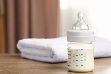 Photo of Feeding bottle with milk and soft towel on wooden table indoors. Space for text