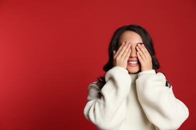 Beautiful young woman covering her eyes on red background, space for text. Christmas party