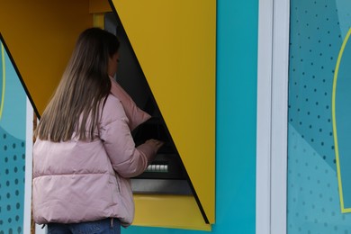 Photo of Woman using modern cash machine outdoors, back view