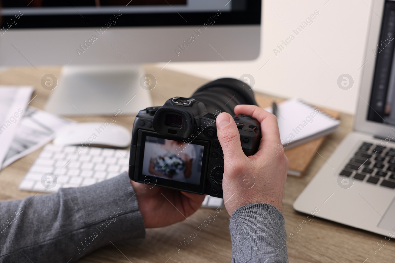 Photo of Professional photographer with digital camera at wooden table indoors, closeup