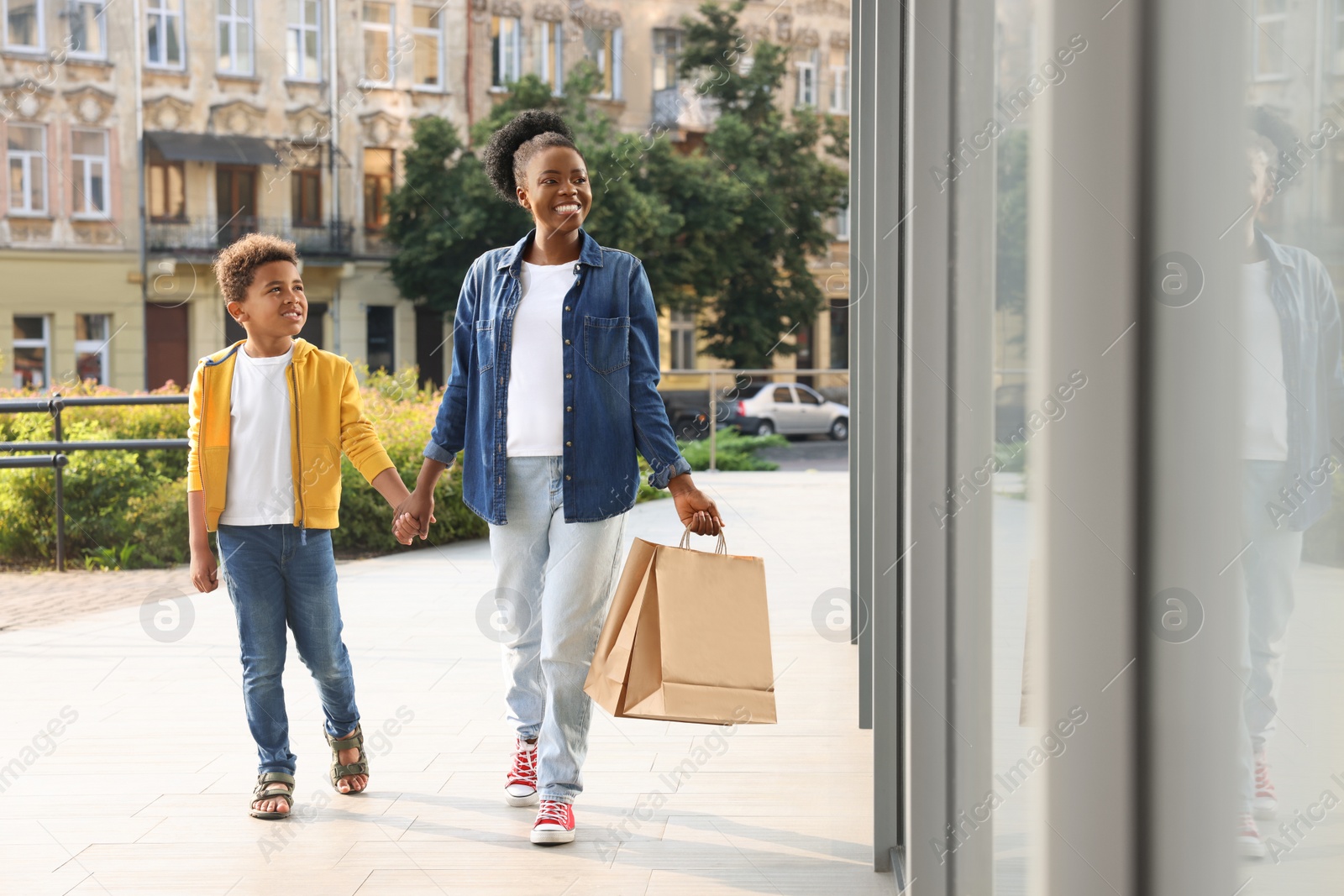 Photo of Family shopping. Happy mother and son with purchases near mall outdoors