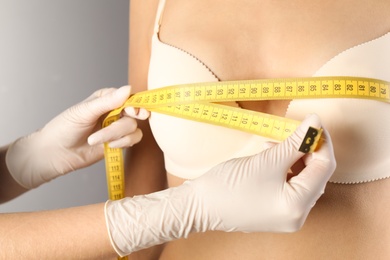 Photo of Doctor measuring size of patient's breast on gray background, closeup. Cosmetic surgery