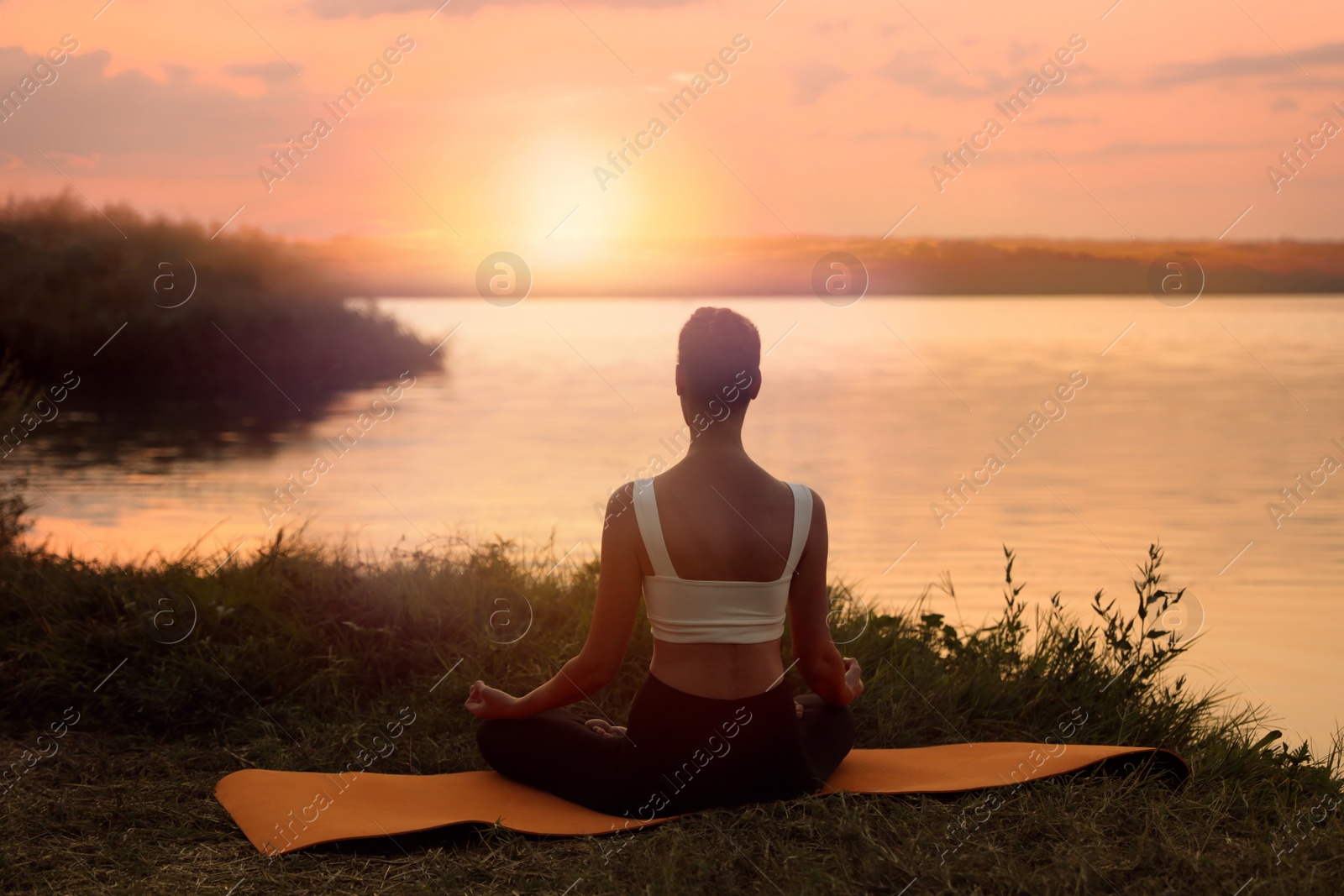 Photo of Woman meditating near river in twilight, back view