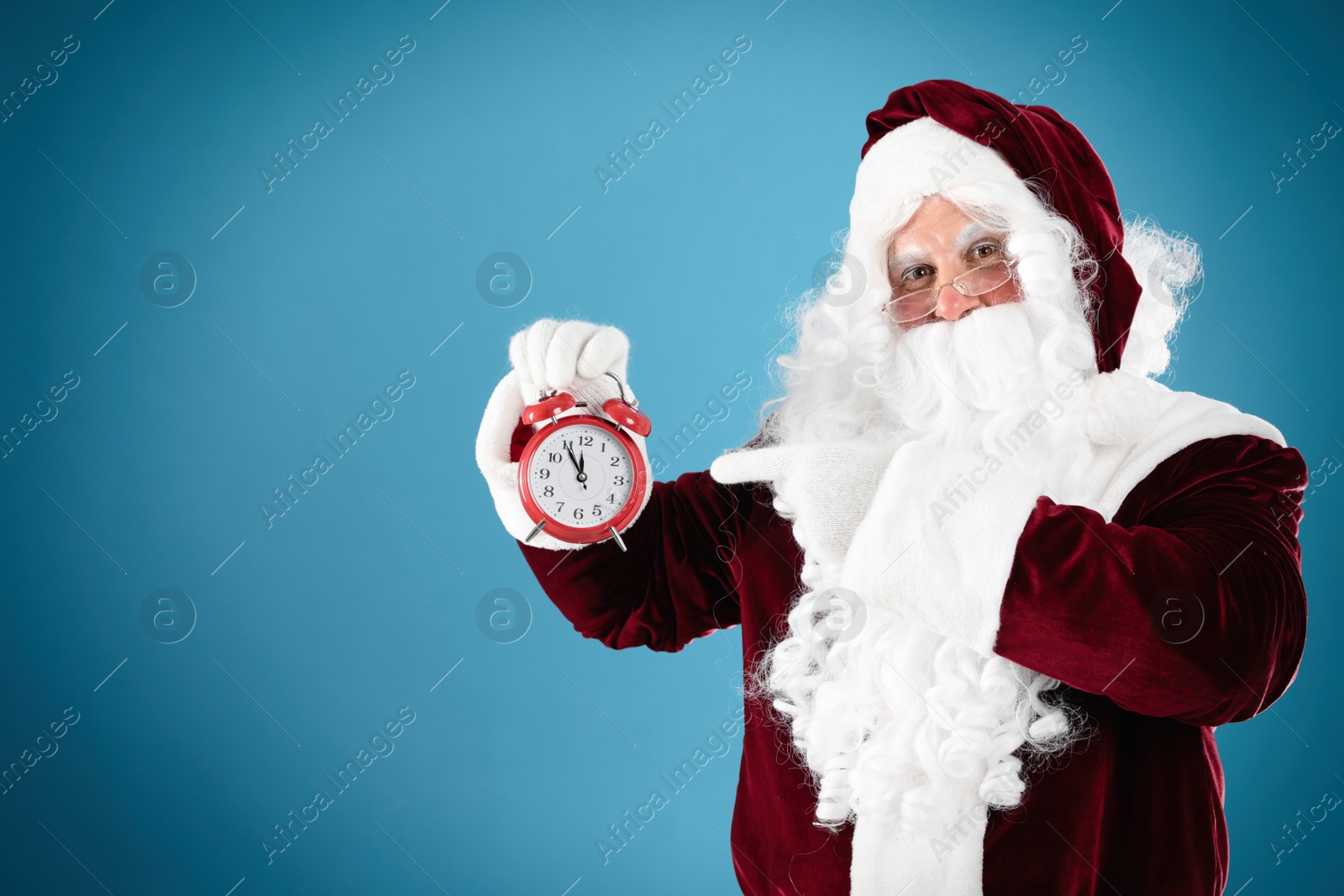 Photo of Santa Claus holding alarm clock on blue background, space for text. Christmas countdown