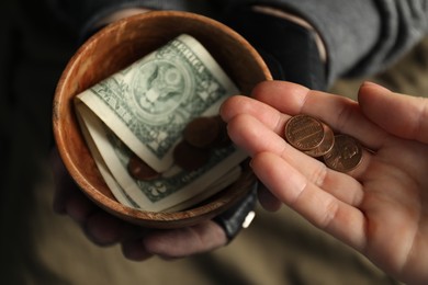 Photo of Woman giving coins to poor homeless man with bowl of donations, closeup