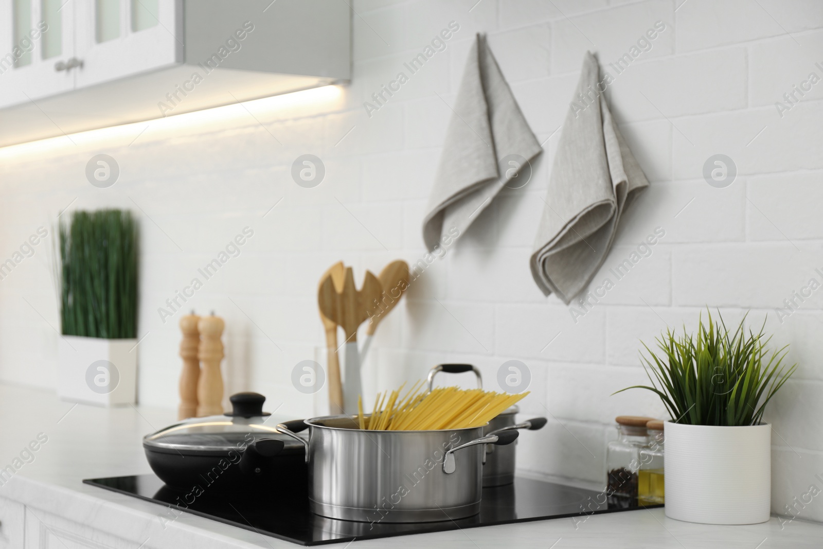 Photo of Pot with uncooked pasta and frying pan on stove in kitchen