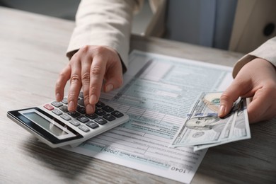 Payroll. Woman with dollar banknotes and calculator planning budget at wooden table, closeup