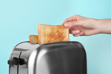 Photo of Woman taking slice of bread from toaster on light blue background, closeup