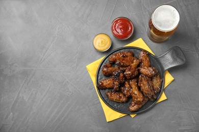 Photo of Tasty roasted chicken wings, sauces and glass of beer on black table, flat lay. Space for text