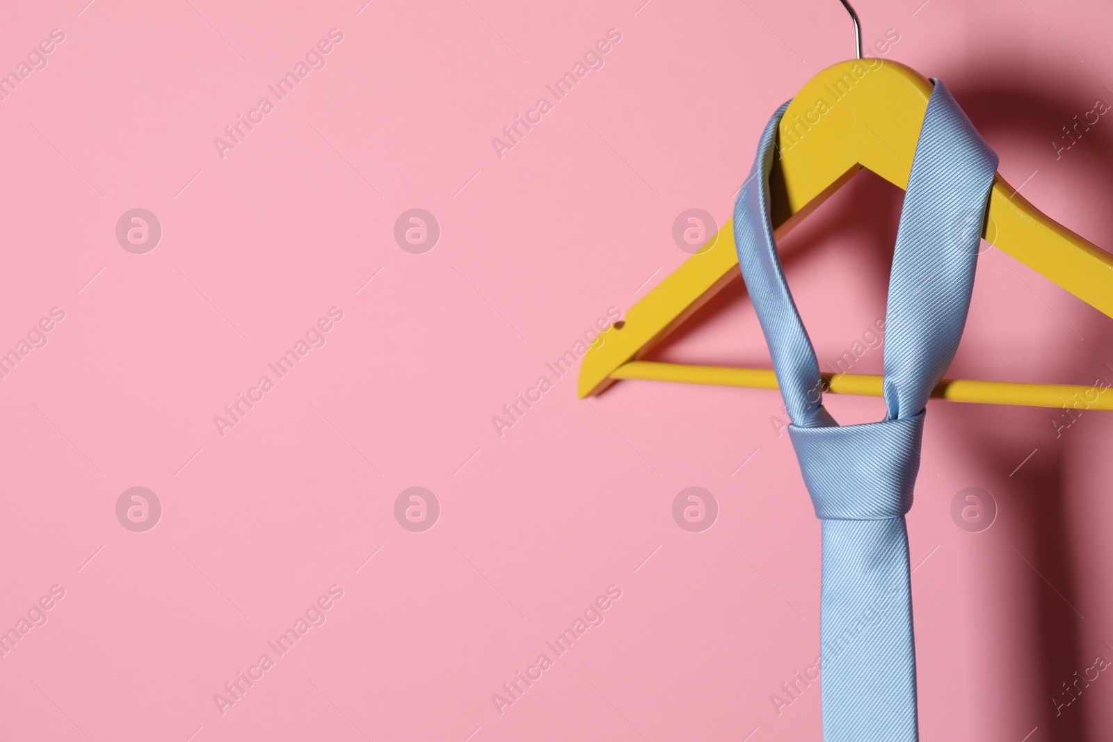 Photo of Hanger with light blue tie on pink background. Space for text