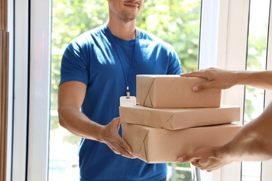 Photo of Young courier giving parcels to client in doorway, closeup