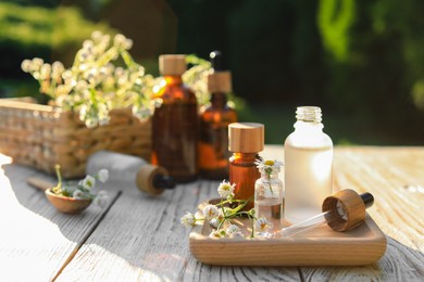 Chamomile essential oil, pipette and flowers on white wooden table outdoors, space for text