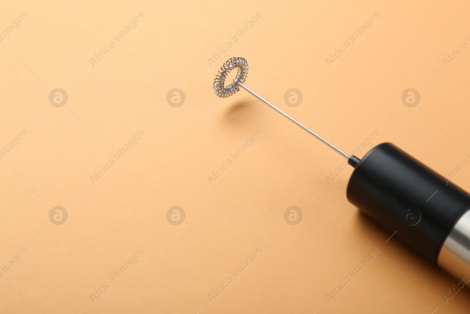 Photo of Milk frother wand on pale orange background, closeup. Space for text