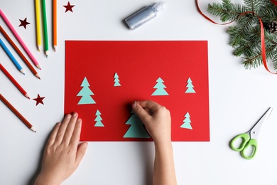 Little child making Christmas card at white table, top view