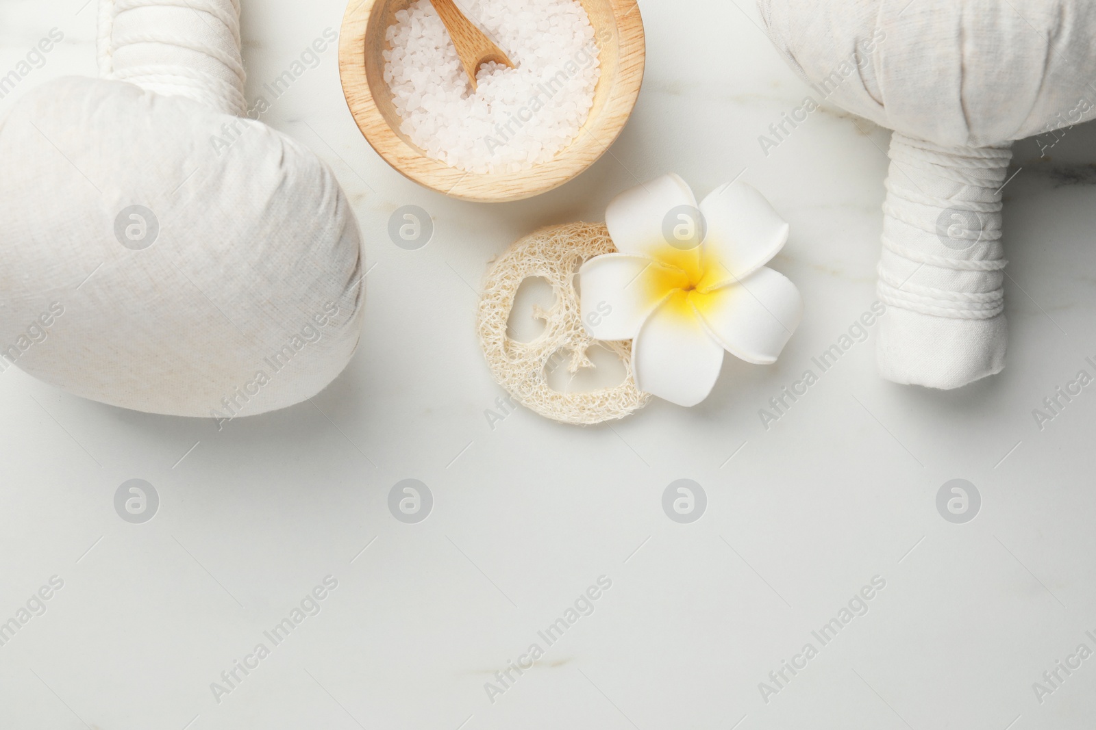 Photo of Flat lay composition with spa bags, sea salt and plumeria flower on white marble table. Space for text