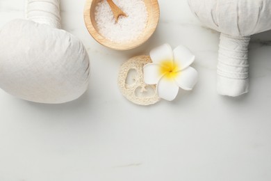 Photo of Flat lay composition with spa bags, sea salt and plumeria flower on white marble table. Space for text