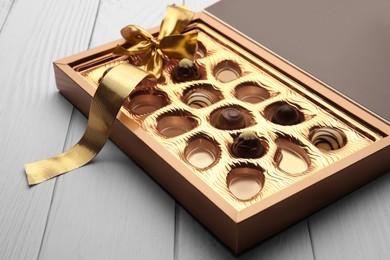 Photo of Partially empty box of chocolate candies on white wooden table