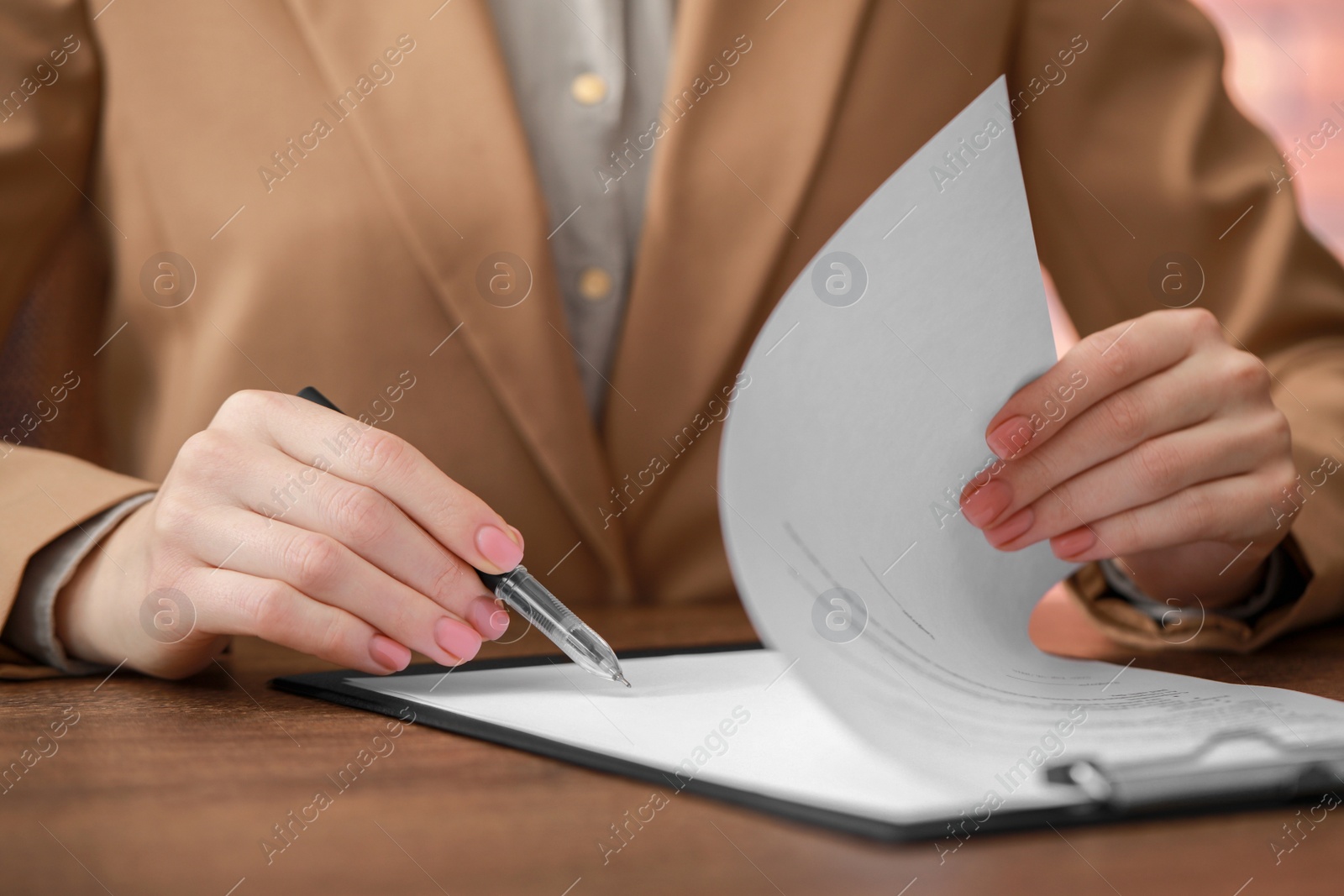 Photo of Woman signing documents at wooden table in office, closeup