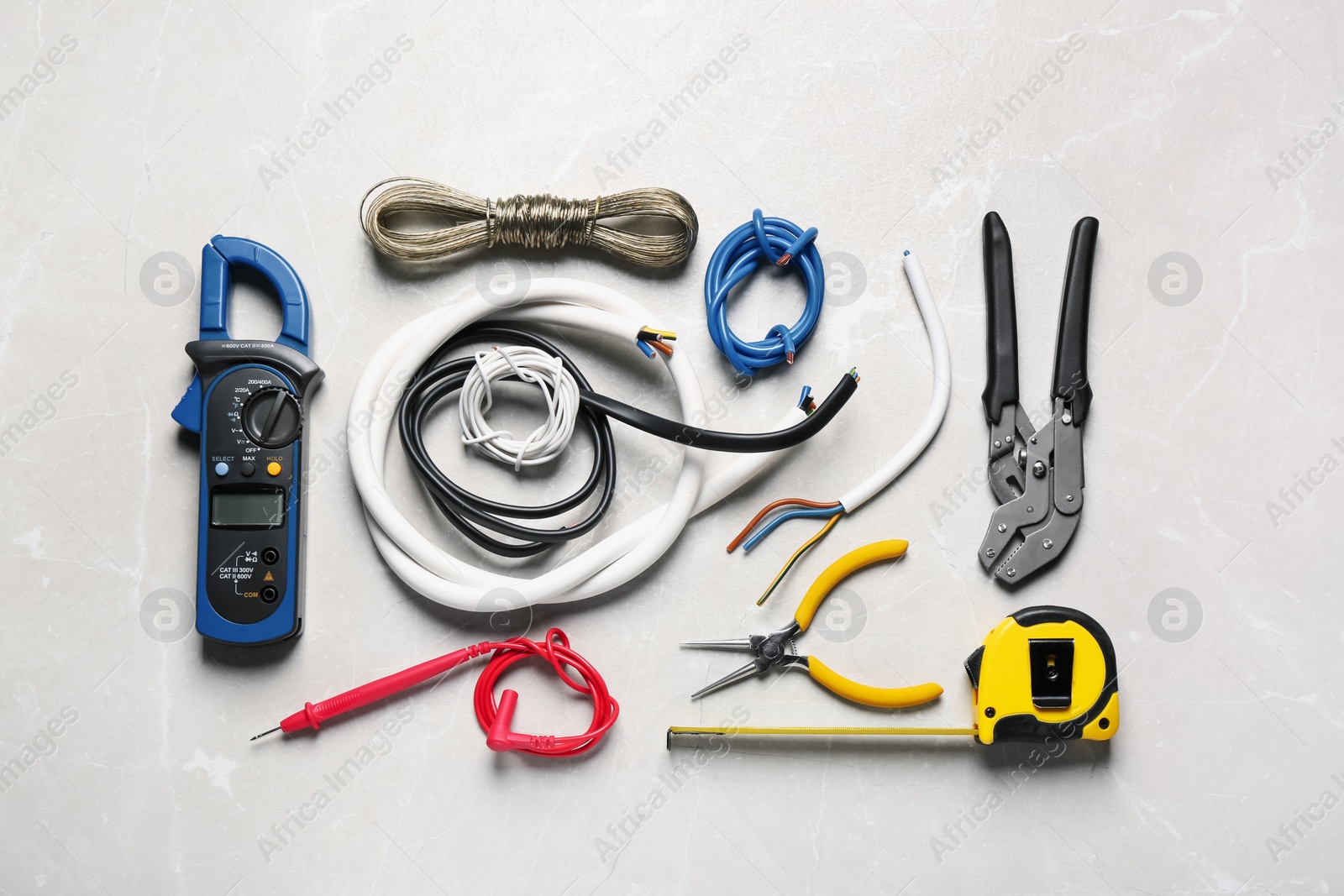 Photo of Different wires and electrical tools on light grey marble table, flat lay