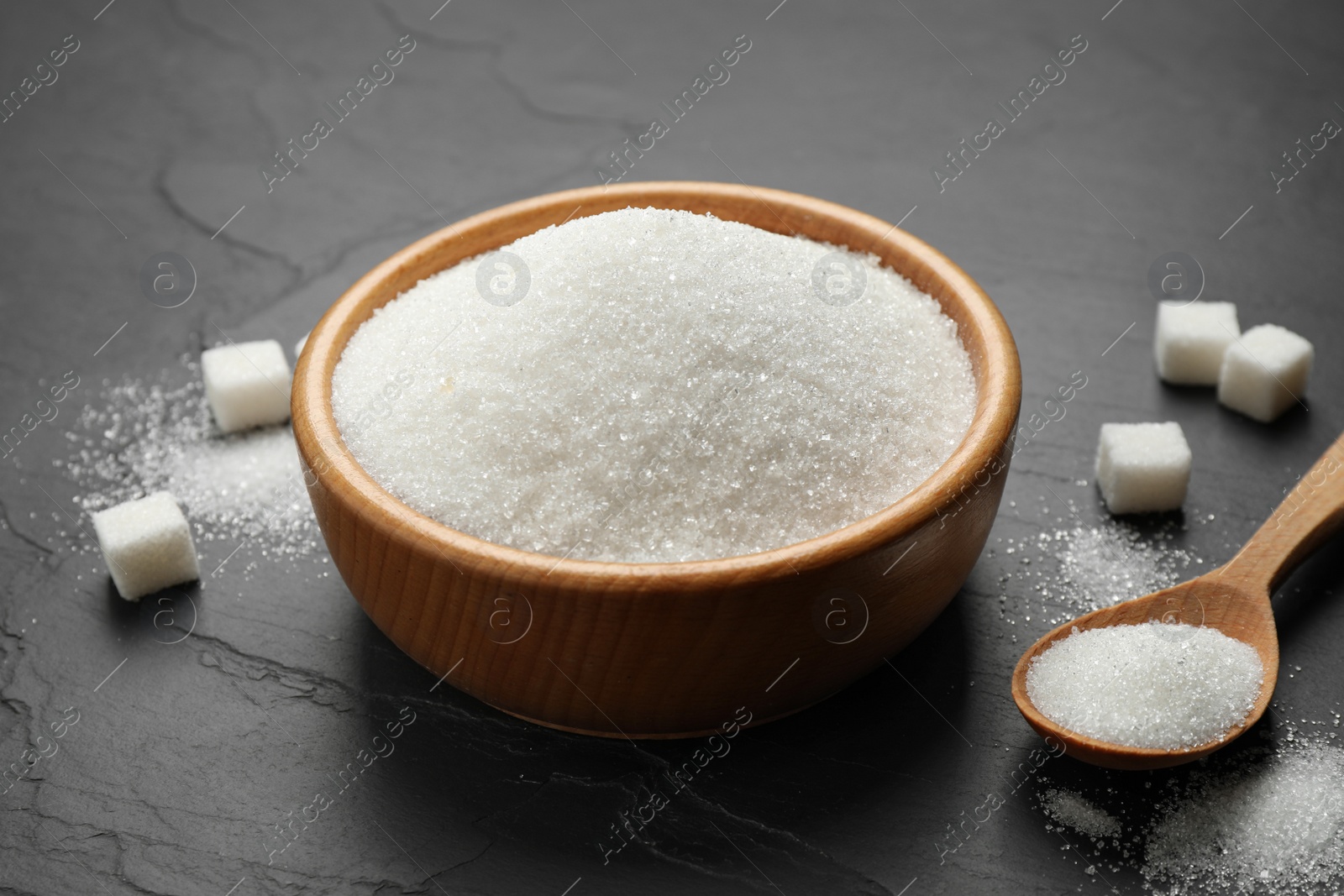 Photo of Granulated sugar in bowl on dark table