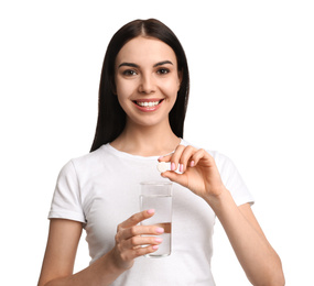 Young woman with glass of water and vitamin pill on white background