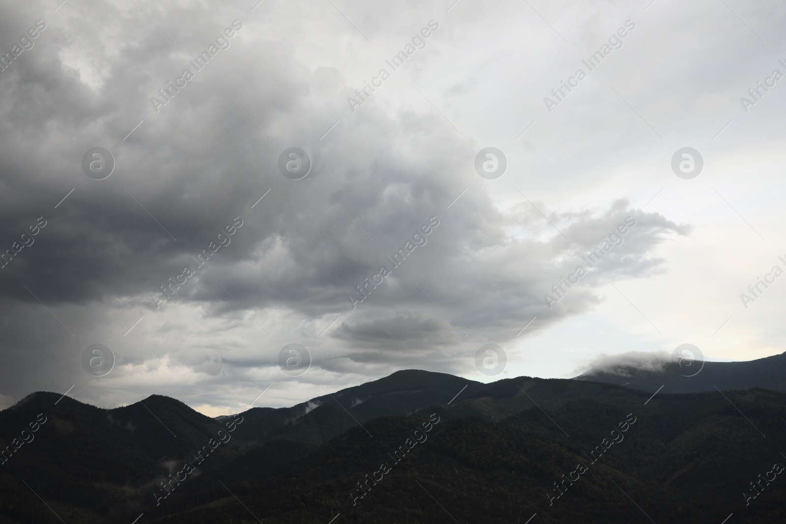 Photo of View of sky with grey thunder clouds over mountains