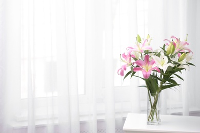 Photo of Vase with bouquet of beautiful lilies on white table indoors. Space for text