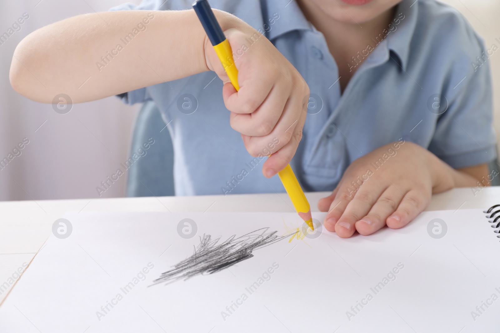 Photo of Little boy drawing with pencil at white table indoors, closeup. Child`s art