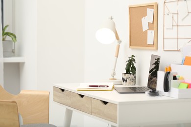 Photo of Home workspace. Modern laptop, lamp and stationery on wooden desk in room