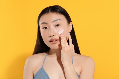 Beautiful young woman with sun protection cream on her face against orange background