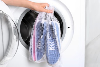 Woman putting pair of sport shoes in mesh laundry bag into washing machine, closeup