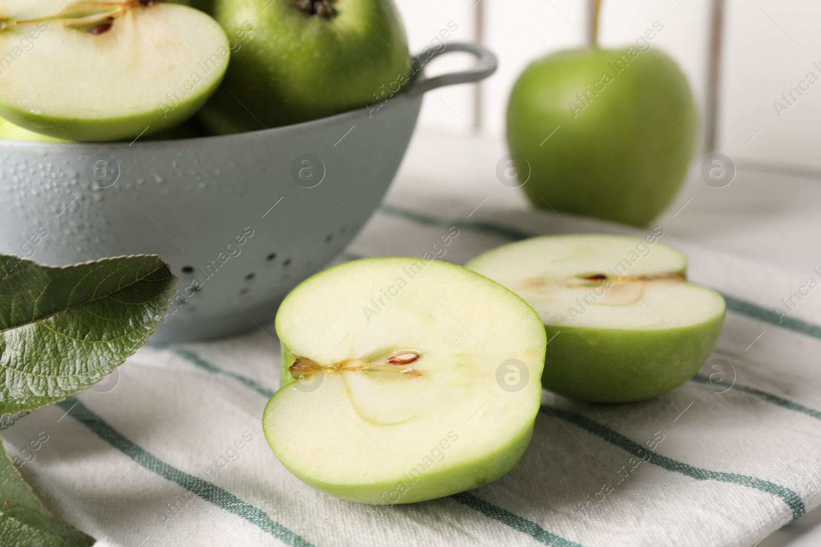 Photo of Fresh green cut apple and leaves on white striped tablecloth, closeup