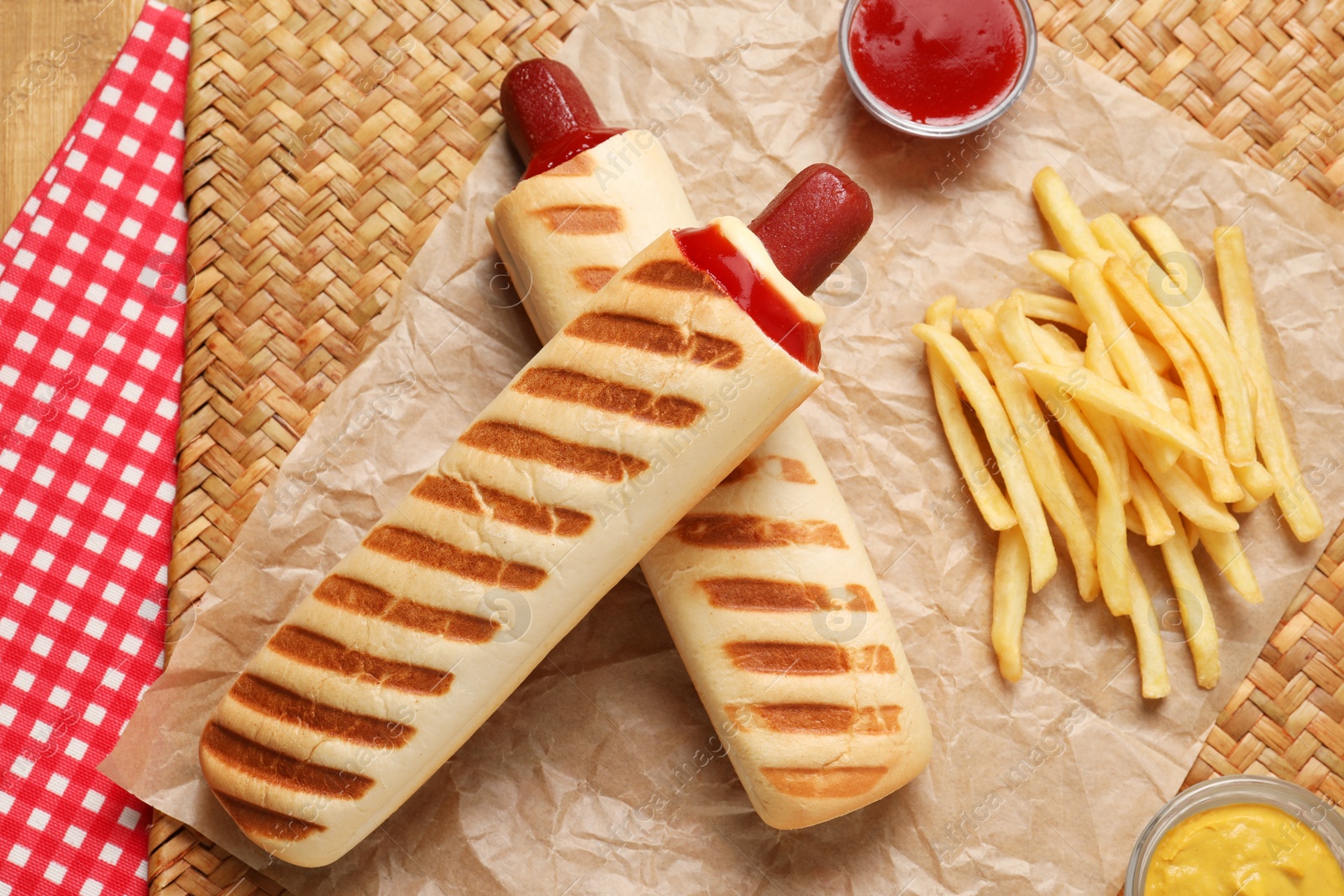Photo of Delicious french hot dog, fries and dip sauce on wicker mat, flat lay
