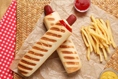 Photo of Delicious french hot dog, fries and dip sauce on wicker mat, flat lay