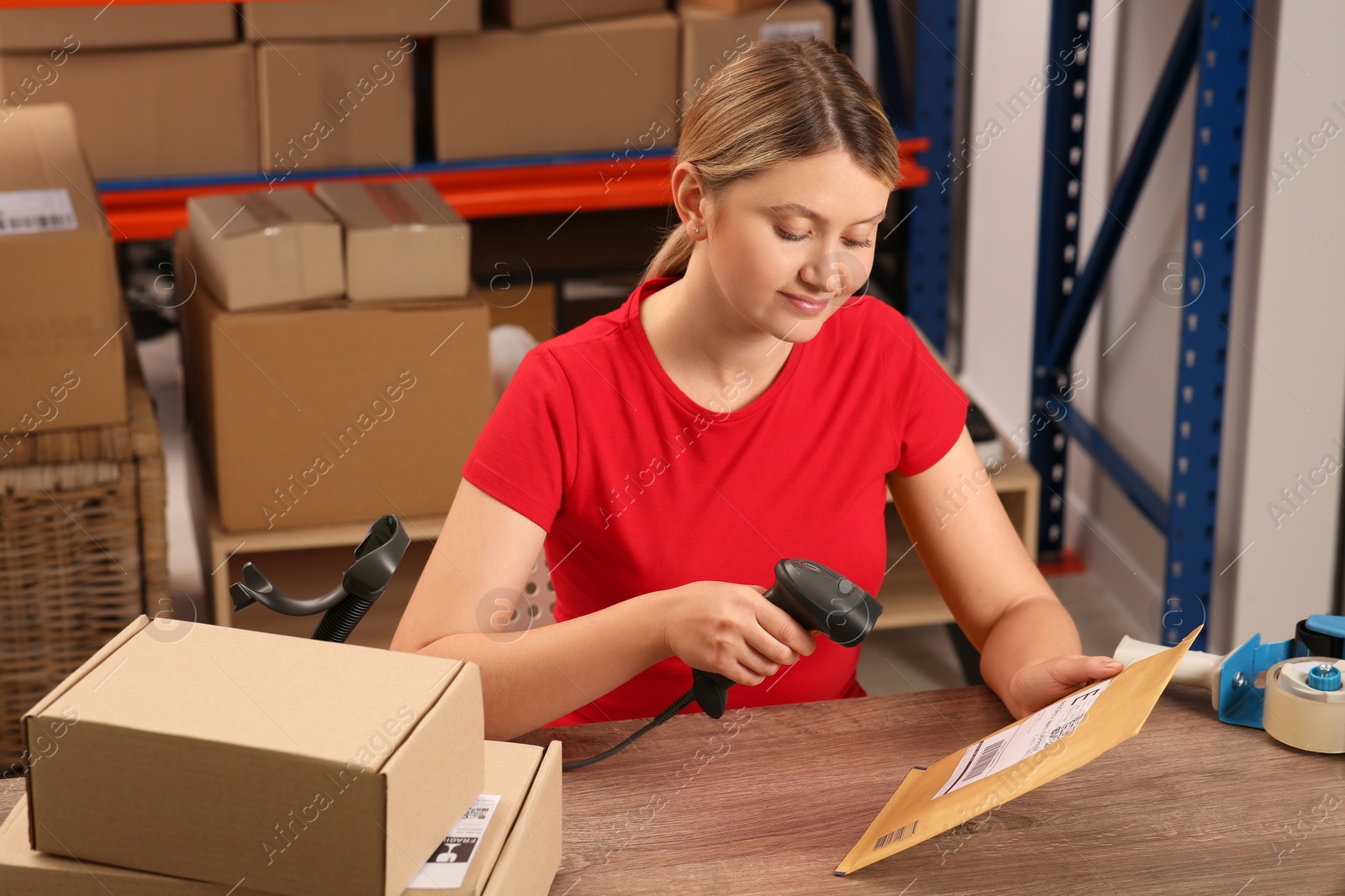 Photo of Post office worker with scanner reading parcel barcode at counter indoors