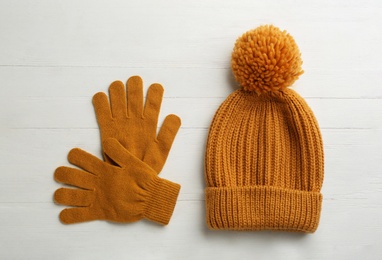Woolen gloves and hat on white wooden background, flat lay