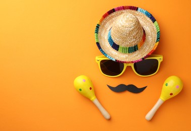 Photo of Mexican sombrero hat, sunglasses, fake mustache and maracas on orange background, flat lay. Space for text