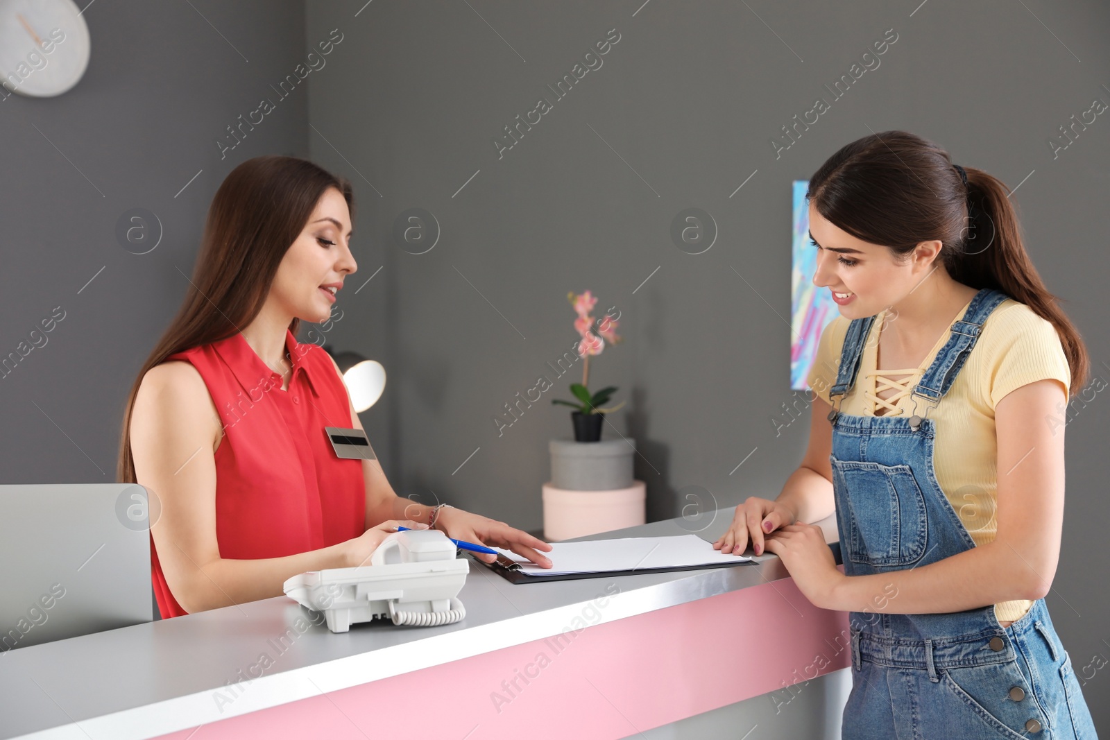 Photo of Young receptionist working with client at desk in beauty salon