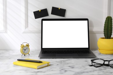 Office workplace with computer, glasses, houseplant and stationery on marble table near white wall