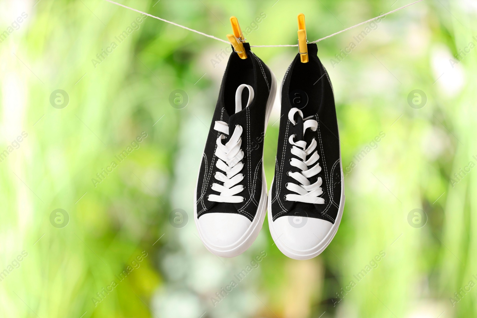 Photo of Stylish sneakers drying on washing line against blurred background