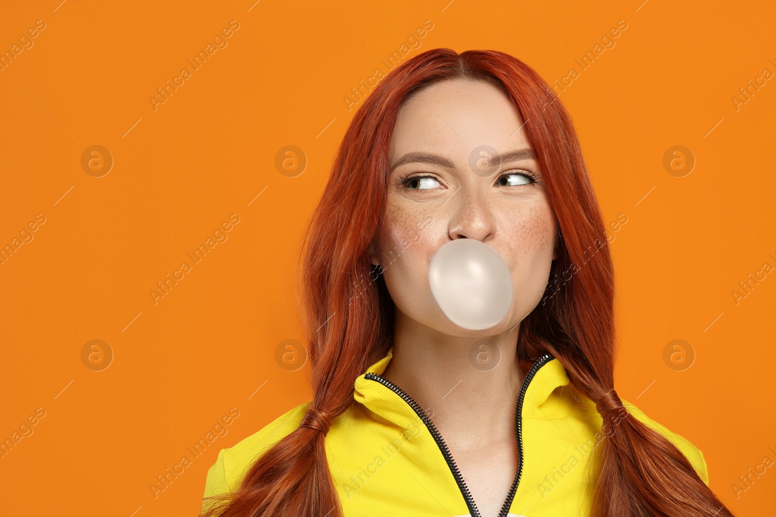Photo of Portrait of beautiful woman blowing bubble gum on orange background. Space for text