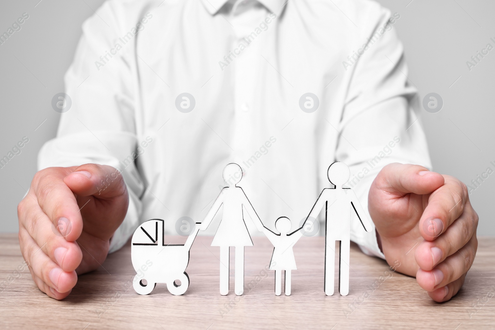 Photo of Man protecting figures of family at wooden table. closeup. Insurance concept