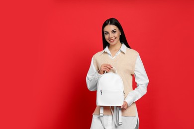 Young woman with stylish backpack on red background. Space for text