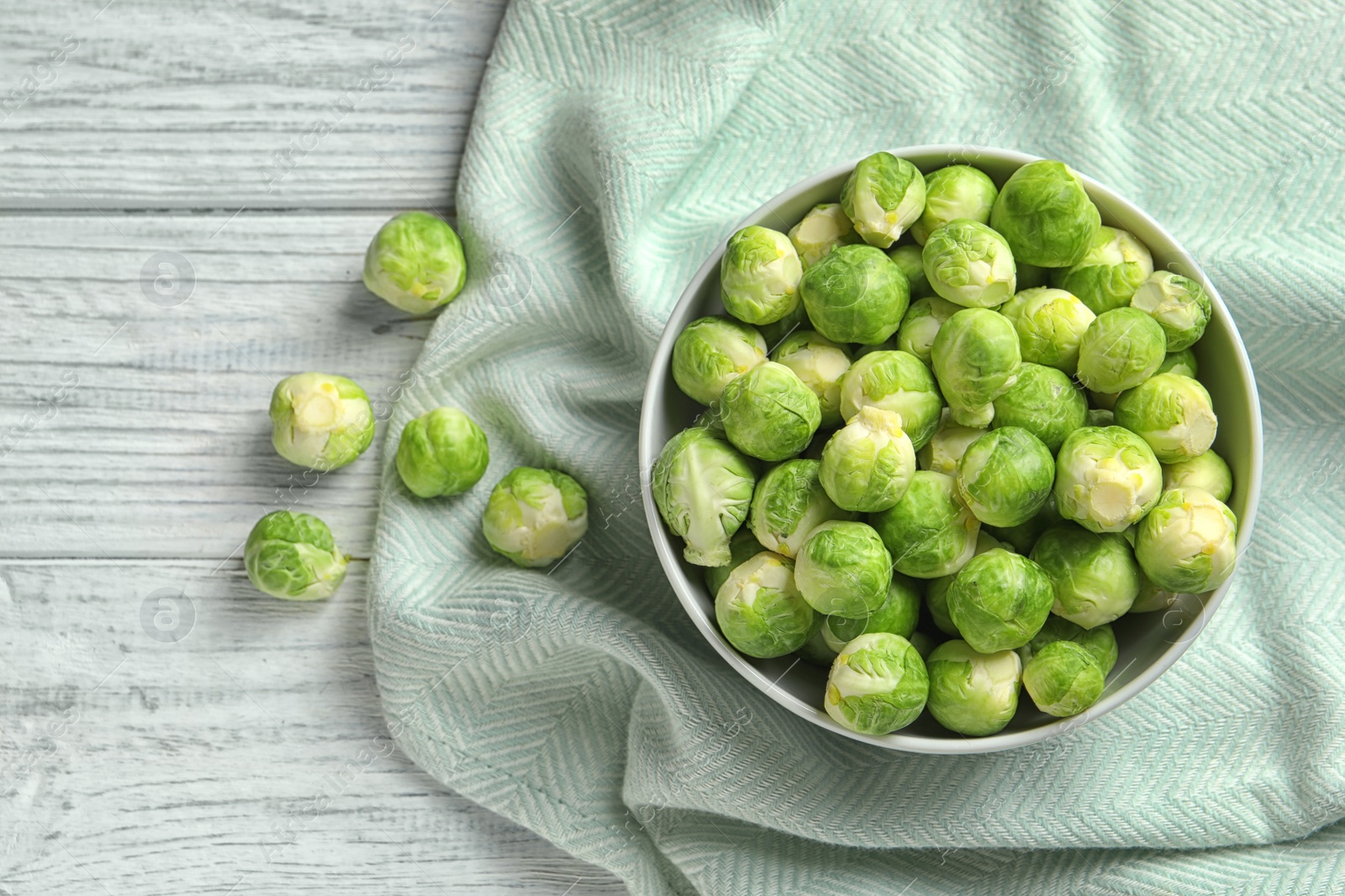 Photo of Bowl of fresh Brussels sprouts and fabric on wooden background, top view. Space for text